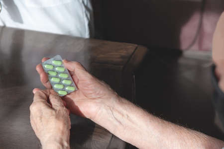 doctor's hand gives an old patient a pill. Gerontology service, nursing home. Unrecognizable people, part of the body.の写真素材