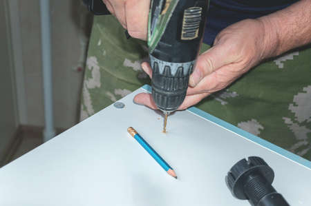 Installation of a plastic foot for the cabinet. the hand of a man repairing furniture in the house.