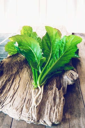 Fresh bunch of lettuce mustard greens on a wooden textured background. Fresh herbs are collected in...