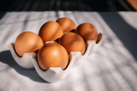 fresh eggs in a white ceramic tray on a wooden rustic table. raw brown eggs in a reusable porcelain...