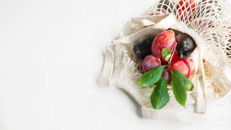 Fresh plums in a reusable mesh shopping bag. Flat surface, autumn background. Ripe organic plums in an eco-bag. Soft focus. concept of zero waste. copy space . bannerの写真素材
