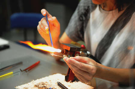 work of a glassblower. Womens hands hold the burner and melt the glass. Soft selective focus, noise.の写真素材