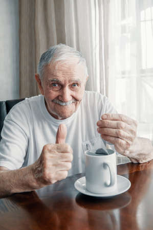 gray-haired, cheerful old man is brewing a tea bag in a cup. Portrait of an old man who drinks tea.
