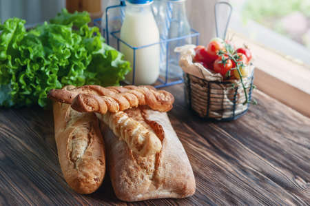 An assortment of different types of bread. Italian ciabatta bread, grissini with tomatoes, milk and olive oil on a rustic table.の写真素材