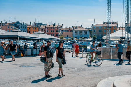 ROVINJ, CROATIA-AUGUST 30, 2018: Tourists walk by the Fountain with a sculpture of a boy and a fish and a clock Tower on the Picturesque Town Square in Rovinj, Croatiaのeditorial素材