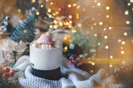 Cozy Christmas still life. The concept of warmth and comfort during the cold winter holidays. cup of coffee or hot chocolate with marshmallows on the Christmas table. glare of the garland adds a festive atmosphere.の写真素材