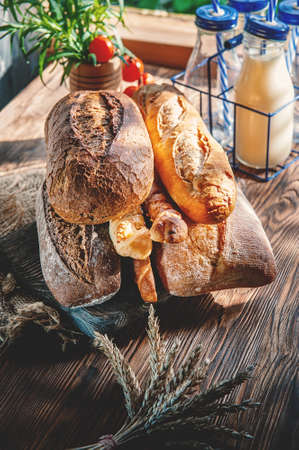 variety of baked goods with milk on a wooden table. various varieties of wheat and rye bread are presented on a wooden relief background.の写真素材