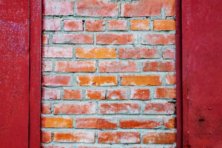 An old authentic brick wall with antique brickwork between metal red doors. Uneven defective...