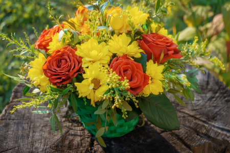 bouquet of flowers is a composition of red roses and chrysanthemums lying on a wooden stump on a...