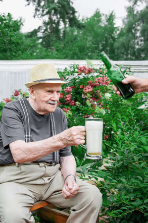 gray-haired old man in a hat with a glass of fresh beer. outdoor recreation after work.の写真素材