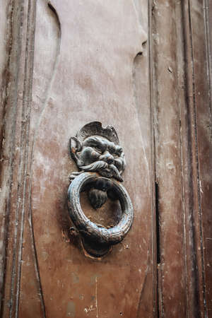 door with a brass knocker in the shape of a man's head, a beautiful entrance to the house. Wooden door detail. decorative element. a door handle in the shape of a face that holds a ring in its teeth.の写真素材