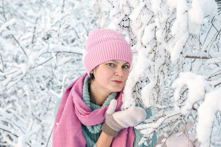 A young woman on the background of a beautiful plant in the snow. A young lady blows a kiss during a snowfall. Great mood, joy, funの写真素材