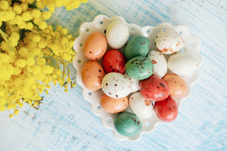 easter eggs with mimosa. Easter holiday mimosa flowers decorated with colorful eggs. Chocolate candies with frosting in the form of quail eggs on a wooden background.の写真素材