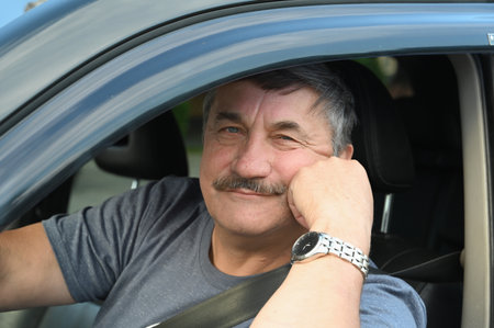 An attractive elderly man smiles as he parks his car. Caucasian elderly people with gray hair and...