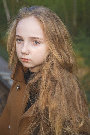 Close-up portrait of a romantic 13-15 year old girl in the woods. A girl with long blond hair looks at the camera.の写真素材
