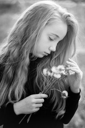 Summer portrait of a romantic girl outdoors with big fluffy dandelions. A 13-year-old girl holds dry dandelions in her hands. Innocence and romance of a young girl. Black and white portrait.の写真素材