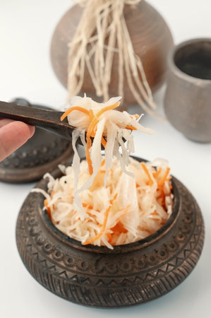 Sauerkraut in a spoon close-up. Sauerkraut in a handmade clay bowl. Horizontal view of cabbage in a clay bowl. traditional home cooking.の写真素材