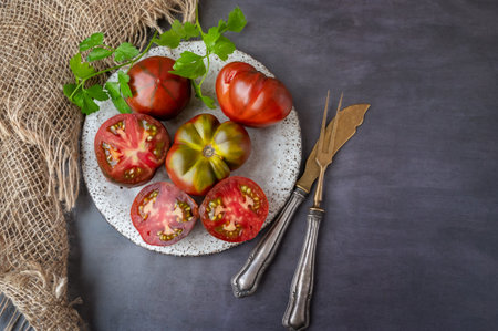 Fresh red ripe tomatoes on wooden cutting board with parsley, dark rustic background. Cut tomatoes with fork and knife. Top view, copy space.の写真素材