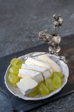 Camembert Brie cheese with grapes in a handmade clay craft plate on a dark background. Side viewの写真素材