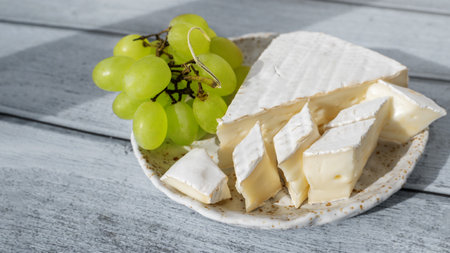 Camembert Brie cheese with grapes in a handmade clay craft plate on a blue wooden background. Side viewの写真素材