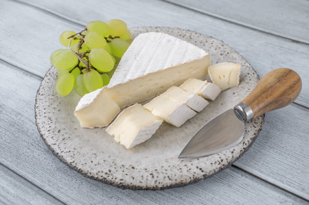 Camembert Brie cheese with grapes in a handmade clay craft plate on a blue wooden background. Side viewの写真素材