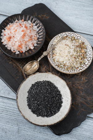 different types of salt. Three different types of salt in handmade craft plates on a clay board. White herbal sea salt, pink Himalayan and black Maldon Thursday.の写真素材