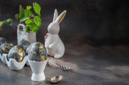Spring Easter still life. White rabbit and eggs painted with gold pattern in a white ceramic stand on a gray background. Easter decor on the table. Copy spaceの写真素材