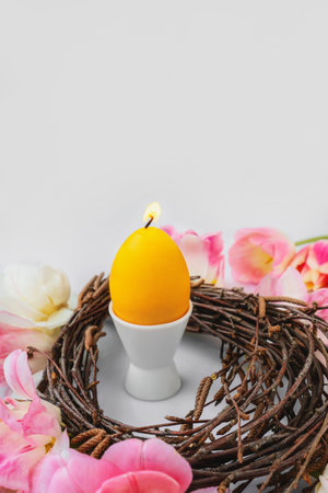 candle in the shape of an egg. Easter, holidays, traditions and object concept - burning candles in the shape of eggs and tulip flowers over a decorative bird's nest. Copy spaceの写真素材