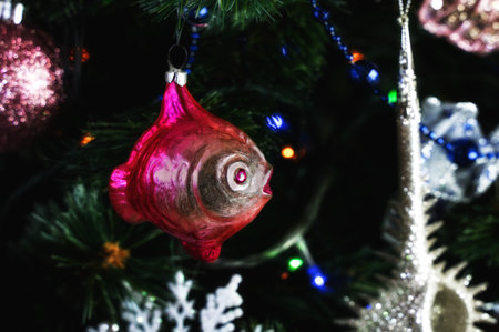 Glass retro Christmas tree toy decorating Christmas tree. Delicate red fish ornament on the Christmas tree with twinkling lights and sparkling tinselの写真素材