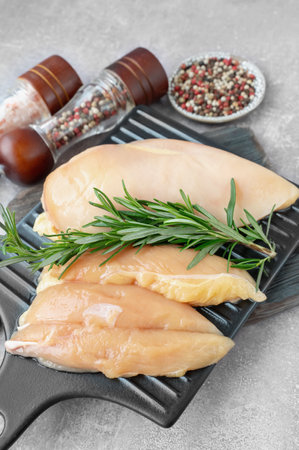 Juicy chicken breast fillets are arranged on a black grill pan along with a sprig of fresh rosemary, ready to be seasoned and cooked in a contemporary kitchen.の写真素材