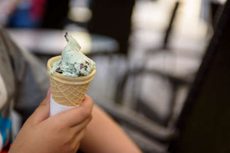 Menthol ice cream with chocolate chips close-up. A child's hand holds a delicious ice cream cone on...