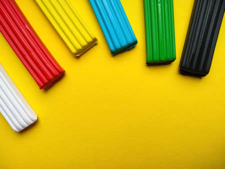 Close-up plasticine of different colors lies on a yellow background with copy space. White, red, yellow, blue, green, black plasticine for children. Children's creativity. Preparation for school. Plasticine modeling.の写真素材
