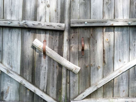 Close-up old wooden rickety gates. Rustic gate made of dry gray planks with rusty handles....