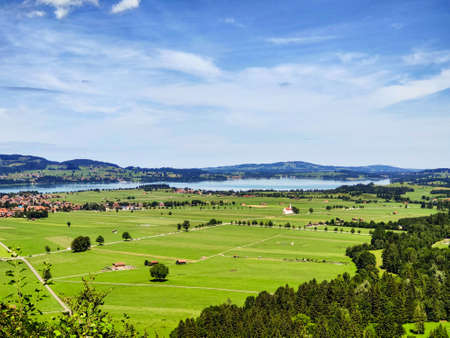 Beautiful green valley with villages, lake, hills and forests in Bavaria, Germany. View of green fields and houses with red roofs near the river against the blue sky. Summer landscape of a small town.の写真素材