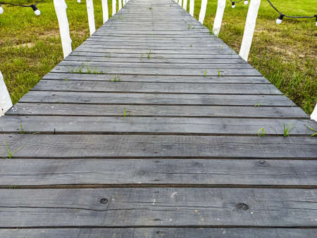 Walkway made of old gray wooden planks with white handrails and white light bulbs. Dock of wooden...