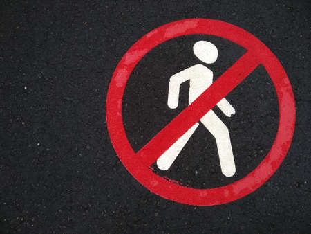 A sign on asphalt prohibiting the movement of pedestrians. Pedestrians are not allowed to walk. Sign of crossed red circle and man on the road after rain with copy space.の写真素材