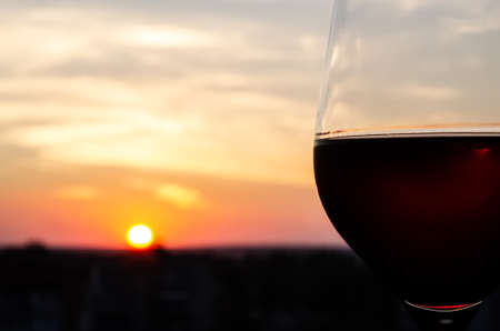 Close-up glass with red wine on a blurred background with copy space. Part of a wine glass on a sunset sky background. Sunset. Beautiful sunset with a glass of wine in the foreground.の写真素材