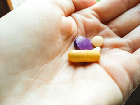 Close-up multi-colored pills in the palm with copy space. Round purple and beige round pills and...