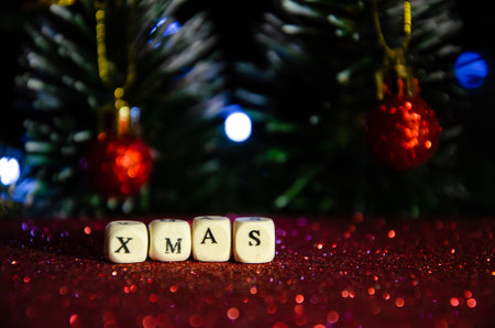 Selective focus letters on cubes Xmas on red shiny background with Christmas tree. The inscription Xmas. Seasonal winter holiday. New year concept. New Year's mood.の写真素材