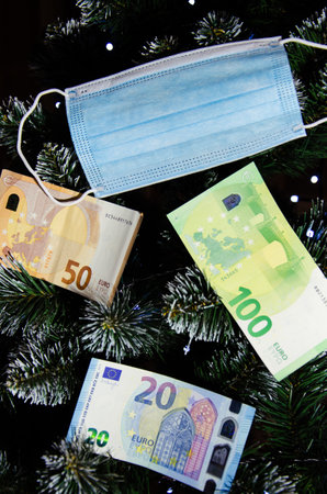 Selective Focus Christmas tree decorated with protective medical mask and Euro banknotes. New reality. Winter quarantine concept with copy space. Corona virus Christmas.の写真素材