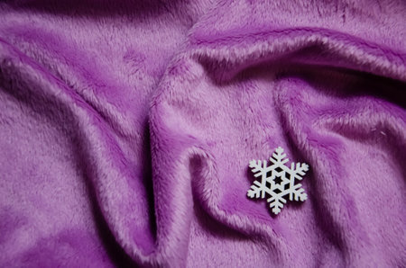 White decorative snowflake on purple plush background with copy space. Winter abstract background. Fluffy fabric surface. Artificial violet fur. Top view, flat lay.の写真素材