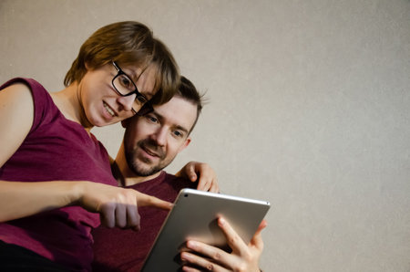 Happy young couple enjoying time online on digital tablet. Caucasian man and woman searching information using laptop at home. Laughing people.の写真素材