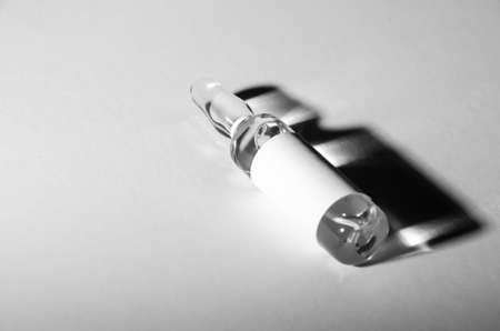 Black and white photo. Selective focus ampoule with medicine with copy space. The vaccine vial lies on white surface and casts dark shadow. Pandemic concept. Health protection.の写真素材