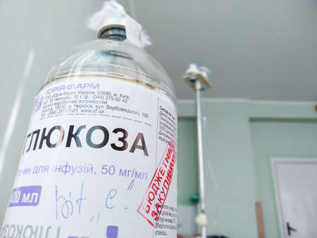 Lutsk, Ukraine - February 19 2021. Close up bottle of medical solution "Glucose" and "Budget purchases" against the background of the walls of the hospital ward. Medical theme. Medical equipment. Health care system.のeditorial素材