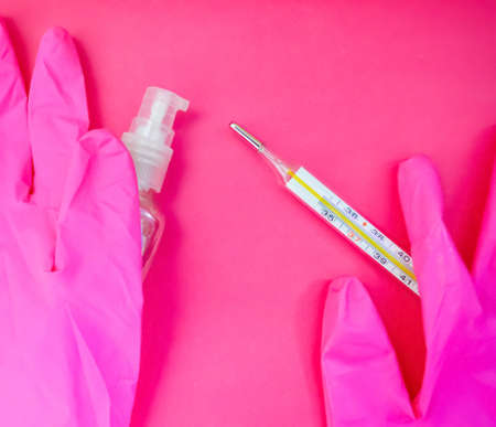 Mercury thermometer, pink medical gloves and sanitizer on pink background with copy space. Medical equipment theme. Health care system background.の写真素材
