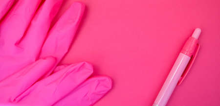 Protective gloves and pen on pink background with copy space. Health care system. Medical theme. Medical equipment.の写真素材