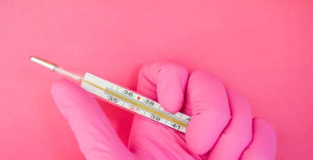 Mercury thermometer in hand of paramedic. Hand in pink glove holds thermometer on pink background with copy space. Health care system. Medical theme. Medical equipment.の写真素材