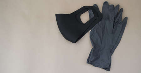 Black protective mask and gloves lie on beige background with copy space. epidemic concept. Top...