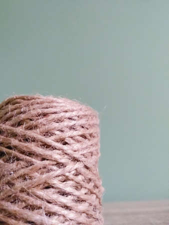 Jute twine in roll on pastel green background. Natural strong thread stands on wooden table with...
