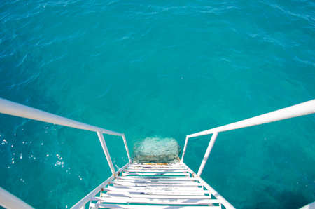 White steps from the pier into the turquoise waters of the Mediterranean. The ladder with handrails is lowered into the water for convenience of tourists. Top view of the sea surface with copy space.の写真素材